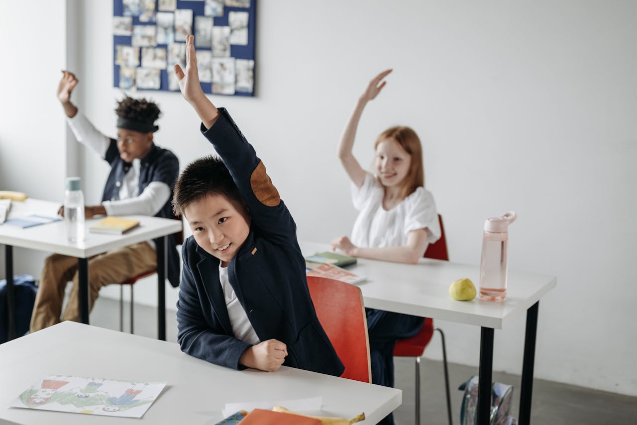 Engaged children in a classroom, eagerly raising hands during a lesson, showcasing diversity and active learning.